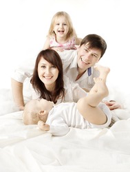 Happy family: parents playing with two kids in bed. Looking at camera. Over white background