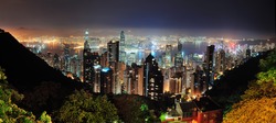 Hong Kong city skyline at night with Victoria Harbor and skyscrapers illuminated by lights over water viewed from mountain top.