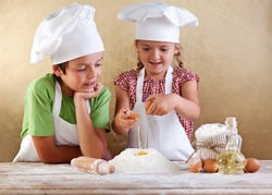 Kids with chef hats preparing a cake or pizza dough - breaking the eggs in the flour heap