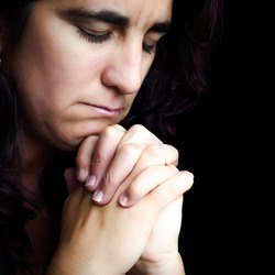 Close-up of an hispanic woman praying with a sad face isolated on black