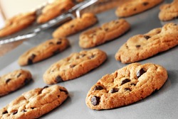 Freshly baked chocolate chip cookies on non-stick cookie sheet with cooling rack in soft focus in background. Macro with extremely shallow dof.