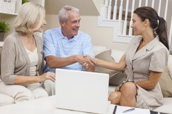 A saleswoman with laptop computer shaking hands with a senior couple at home