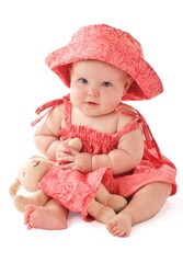 Smiling 6 month old baby girl sits holding a stuffed toy bunny rabbit. Baby's strawberry pink floral hat and sun dress match the toy. Vertical, copy space, isolated on white.