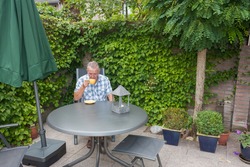 Retired senior Dutch man in deep thoughts whilst drinking a cup of hot coffee in his back yard