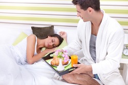 Portrait of happy young man serving breakfast for his girlfriend in bed at home