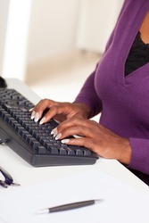 Beautiful African American female executive with dark brown hair at work in an office setting wearing a purple sweater.