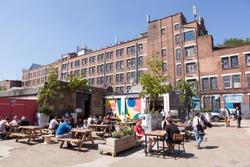 PECKHAM, UK - MAY 19, 2018: People drinking and hanging around outside a bar in the trendy Copeland Park in South London. The Bussey Building is in the background.