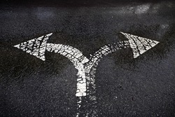 A bi-directional arrow symbol on a wet asphalt road for the concept of choice at a junction.