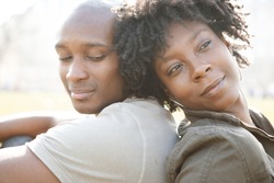 Young african american couple sitting back to back while visiting London on vacation, smiling.