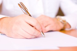 Businessman sitting at office desk signing a contract - focus on right hand with a pen