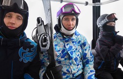 Three skiers in helmets ride on funicular in mountains. Focus on middle man.