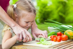sliced cucumber. Mother teaches daughter knife cut cucumber
