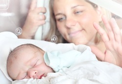 Newborn baby boy sleeping in a incubator. His mother looking at. Close up with shallow DOF.