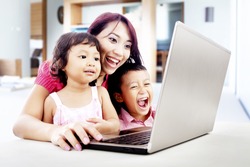 Happy young mother with her children using ultrabook laptop computer in their house