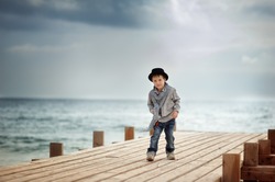 Stylish boy in a hat standing on a wooden bridge on the background of the sea