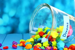 Scattered pieces of paper and colored stones with dreams in glass vase on blue wooden table on blue background