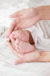 Newborn baby sleeping together with his mother in the bed on white sheets. Mothers hand holding baby. Selective focus on babys head