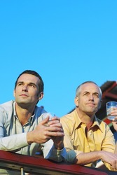 Low angle view of two men leaning on the railing of a patio enjoying a drink