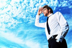 Successful business man standing over blue sky and purposefully looking away.