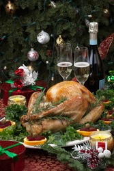Christmas-decorated table with feast, gifts, roasted turkey, candles, champagne, and Christmas tree on back.