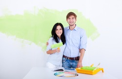happy young couple paint in green color white wall of their new apartment home