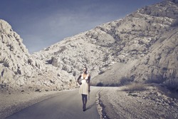Beautiful black girl, with a white dress, walking on a long road of mountains
