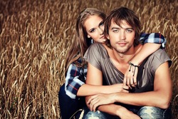 Romantic young couple in casual clothes sitting together in a wheat field.
