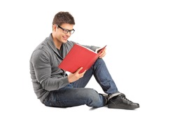 Smiling guy sitting on a floor and reading a book isolated on white background