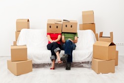Couple in their new home with cardboard boxes, sitting on covered sofa