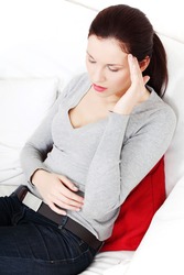 Beautiful young woman having a headache, sitting on a couch and holding her hand next to the head.