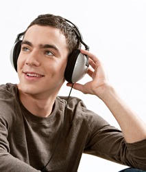 Attractive young man listening to music with his headphones while sitting down, isolated against a white background.
