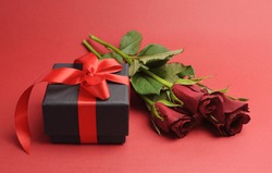 Happy Valentines Day black box with red ribbon gift and red roses, against a red background.