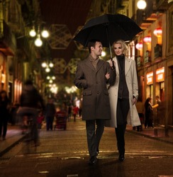 Elegant couple with umbrella outdoors on rainy evening