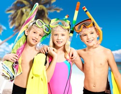 Portrait of the happy children enjoying at beach. Schoolchild kids standing together in bright color swimwear with swimming mask on head .