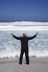 Rear view of a senior businessman standing with arms raised in front of the sea