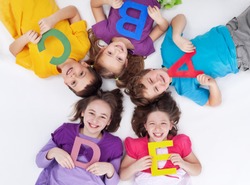 Happy school kids with colorful alphabet letters laying in circle on the floor