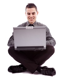 Full length pose of young businessman sitting on the floor and writing on his laptop, isolated on white background