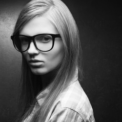 Portrait of a young beautiful blonde model wearing trendy glasses and casual shirt and posing over metal background. Hipster style. Close up. Copy-space. Monochrome studio shot.