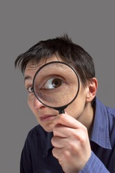 Funny image of a adult woman with a magnifying glass, one eye is enlarged.