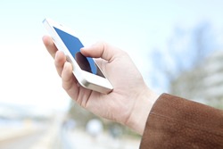 Side view of a woman's hand holding a modern slick smartphone while dialing with her thumb against a blue background.