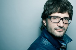 Portrait of a fashionable handsome mature man in blue jacket with striped scarf posing over light blue background. Close-up. Copy-space. Studio shot