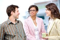 Happy young casual business people standing side by side in fornt of office window, talking and smiling.