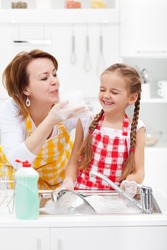 Woman and little girl having fun washing the dishes - playing with the foam