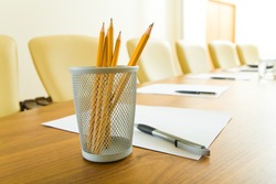 Photo of pencils in plastic glass, some pens and papers on the table in office