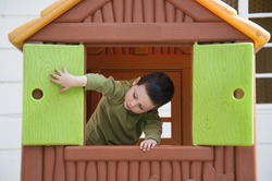 Small child playing with window in a toy playhouse in an yard or an outdoor playground.