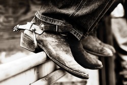 Rodeo cowboys' experienced boots & spurs on an iron rail #2 (shallow focus, high contrast black & white effect)