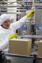 caucasian man worker in white apron, cap and yellow gloves at production line in factory,pressing button at control panel