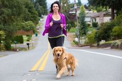 A pretty woman jogging with her golden retriever dog