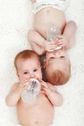 Babies drinking water from feeding bottles - laying next to each other