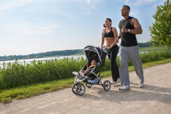 Young Couple Running Outdoor with Little Boy in Stroller Under Morning Sun Light